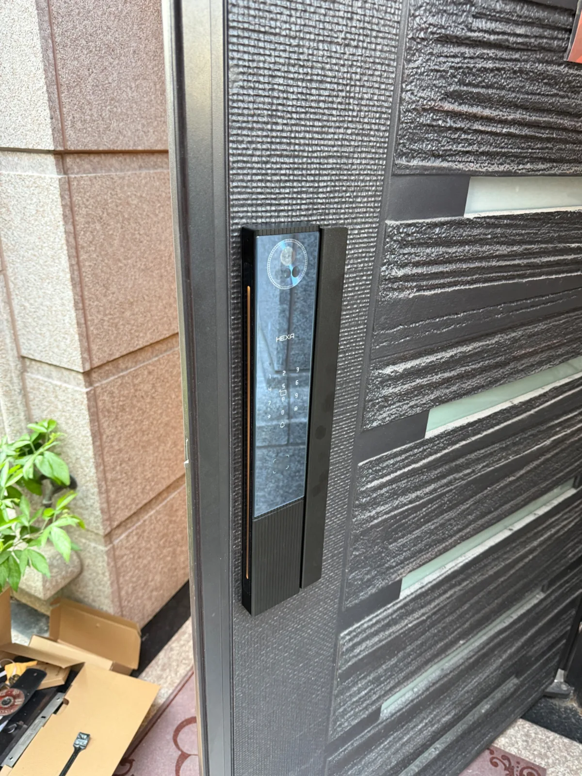 HEXA P200 PRO 的門外側面板亮起觸控數字鍵盤,上方是掌靜脈感應圓框,地上放著安裝用的紙箱與工具