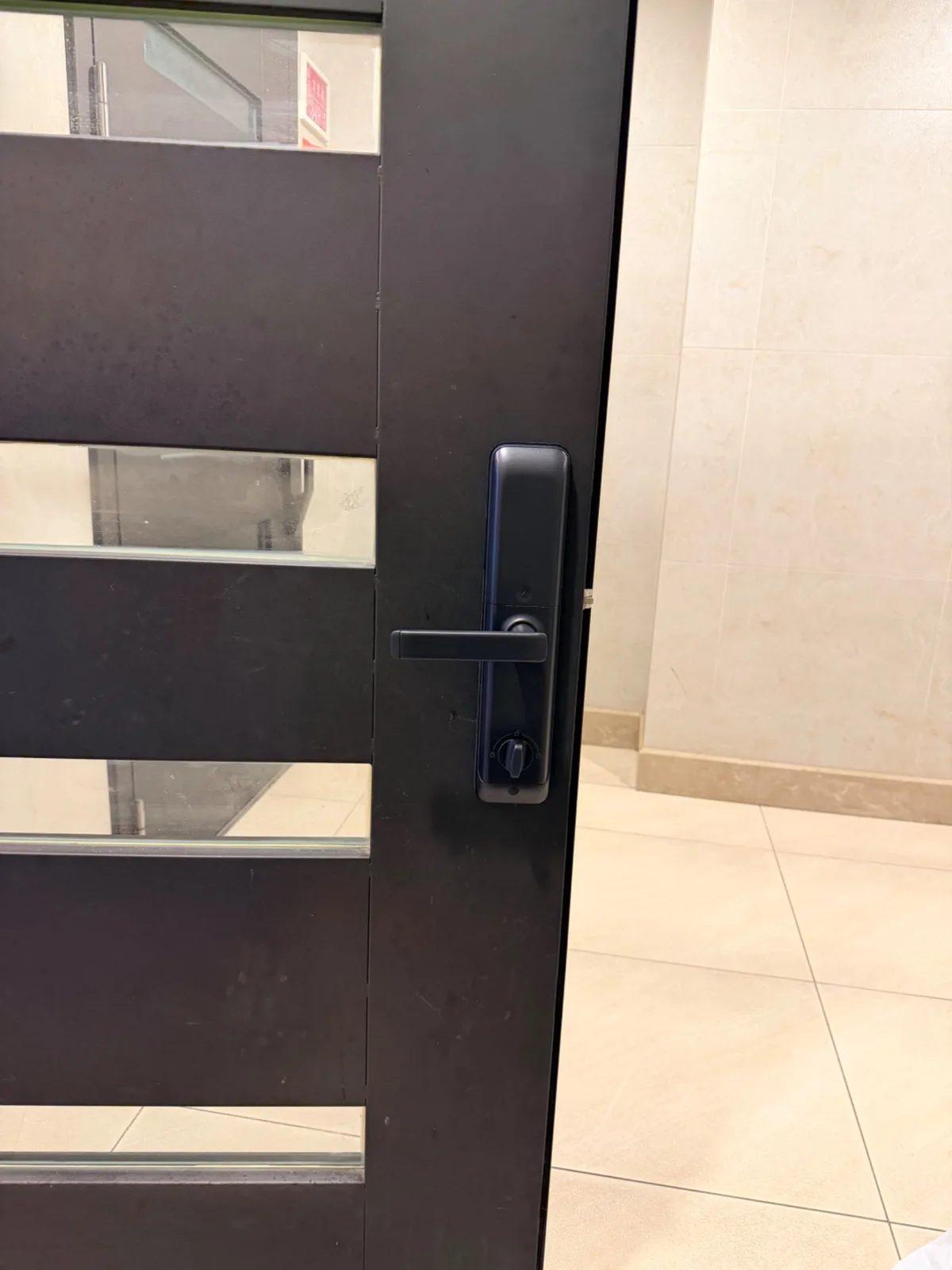 Kwikset PF3 門內側,霧黑機身、水平把手與下方旋鈕,門外是米色磁磚梯廳